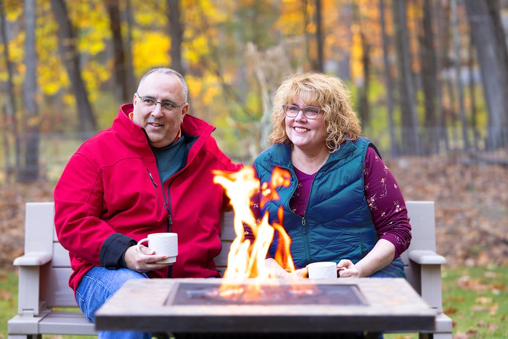 Julie, a real Alpha-1 patient, sitting outside by the fire with her husband.