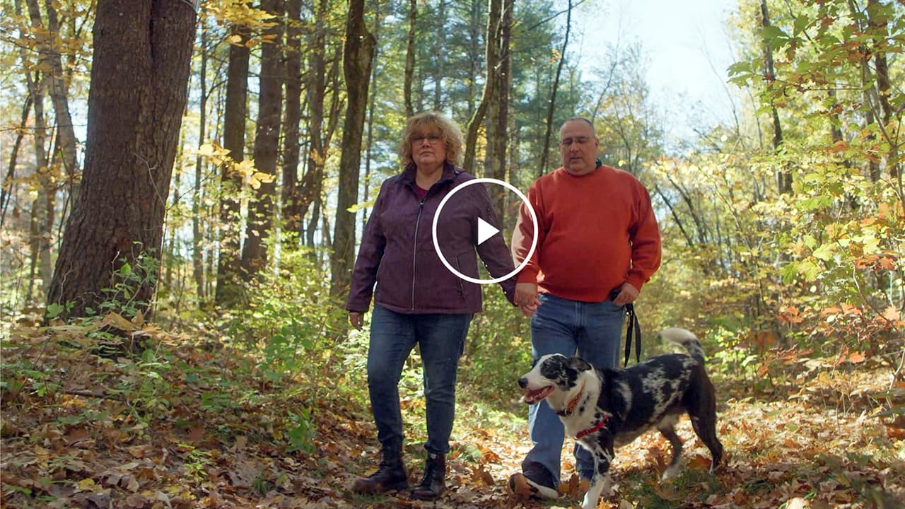 Julie, a real Alpha-1 patient, walking on a trail with her husband and dog.